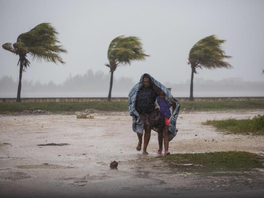 Eine Frau und ein Kind versuchen sich auf Kuba mit einer Decke vor dem peitschenden Regen zu schützen. Foto: Desmond Boylan