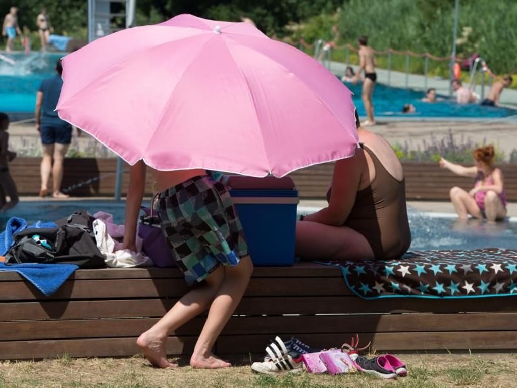 Badegäste im Freibad Wostra in Dresden unter einem Sonnenschirm. Foto: Sebastian Kahnert