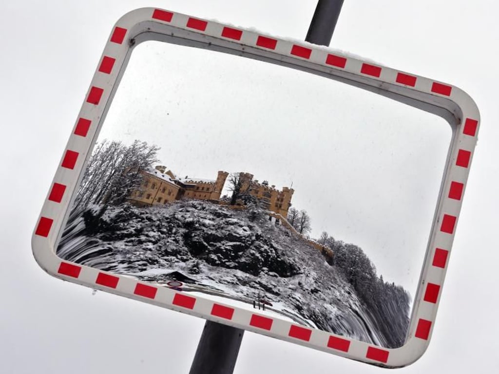 Das in winterlicher Umgebung stehende Schloss Hohenschwangau ist in einem Verkehrsspiegel zu sehen. Der Schneefall im Süden Bayerns wird sich in den nächsten Tagen wieder intensivieren. Foto: Karl-Josef Hildenbrand