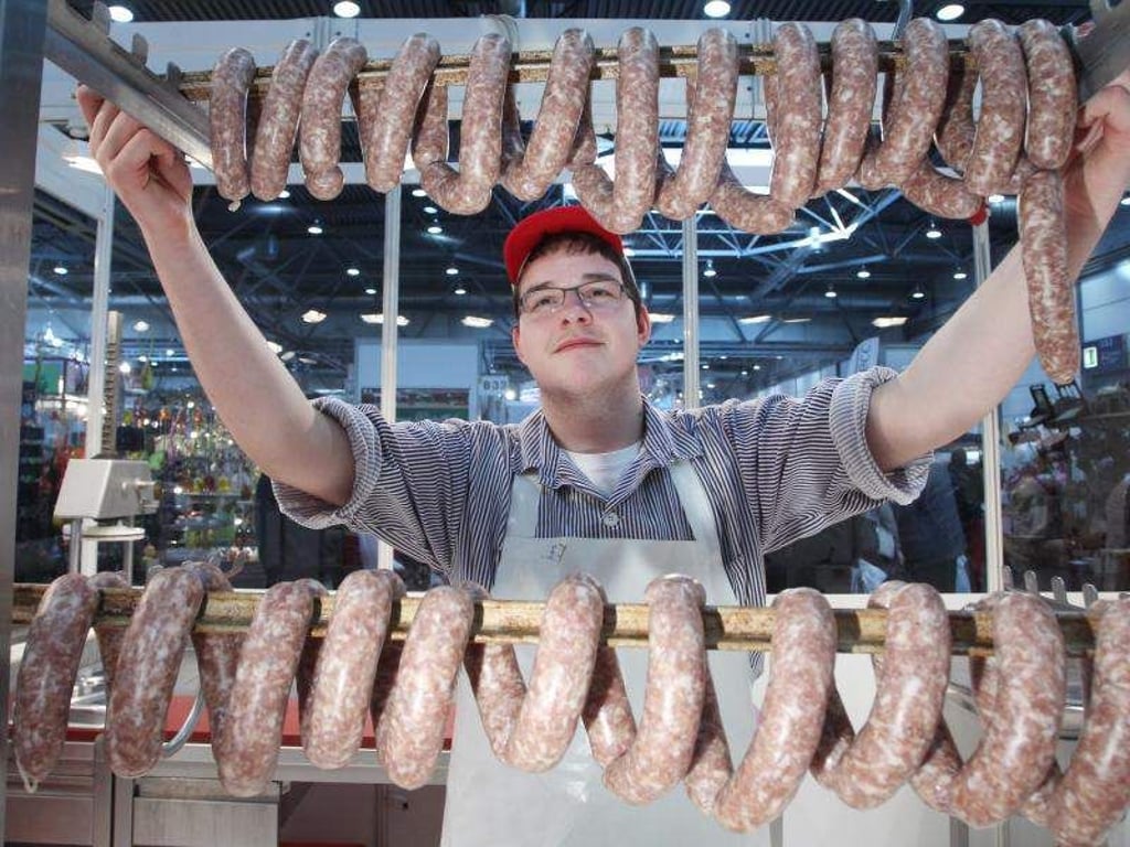 Ein Fleischerlehrling zeigt zur Handwerksmesse frische Knackwürste. Foto: Sebastian Willnow/Archiv