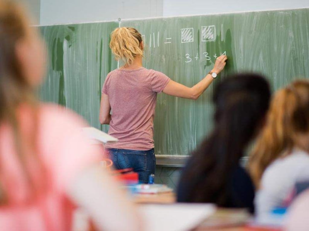 Eine junge Lehrerin schreibt an eine Schultafel im Mathematikunterricht. Foto: Julian Stratenschulte/Archiv