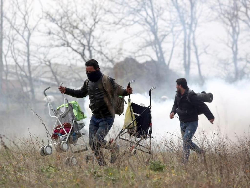 Ein Mann mit zwei Kinderwagen läuft vor Tränengas davon. Foto: Giannis Papanikos/AP