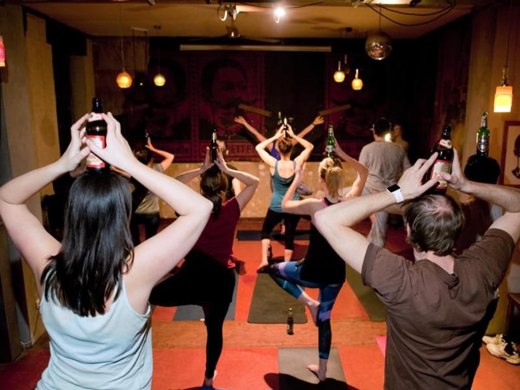 Teinehmer eines Bieryoga-Kurses vollziehen in Berlin in einer Kneipe eine Yogaübung mit Bierflasche. Foto: Klaus-Dietmar Gabbert
