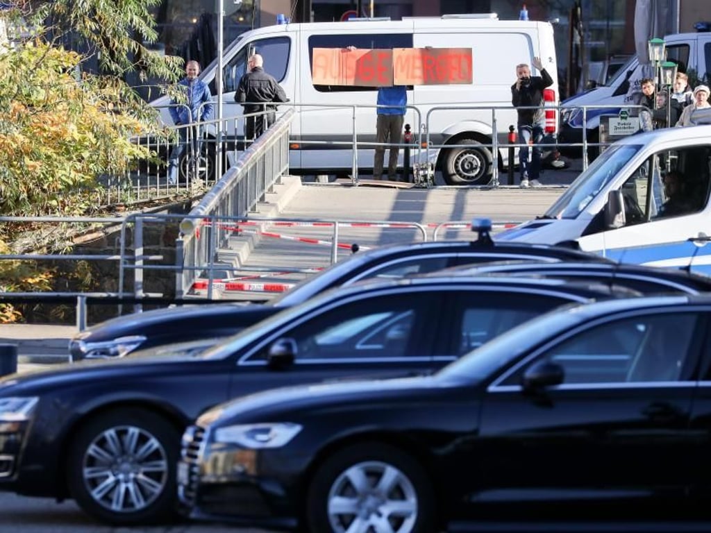 Ein Mann hält in Chemnitz ein selbstgemaltes Pappschild «Ausgemergelt» hinter einer Polizeiabsperrung und den Dienstwagen der Kanzlerin in die Höhe. Foto: Jan Woitas