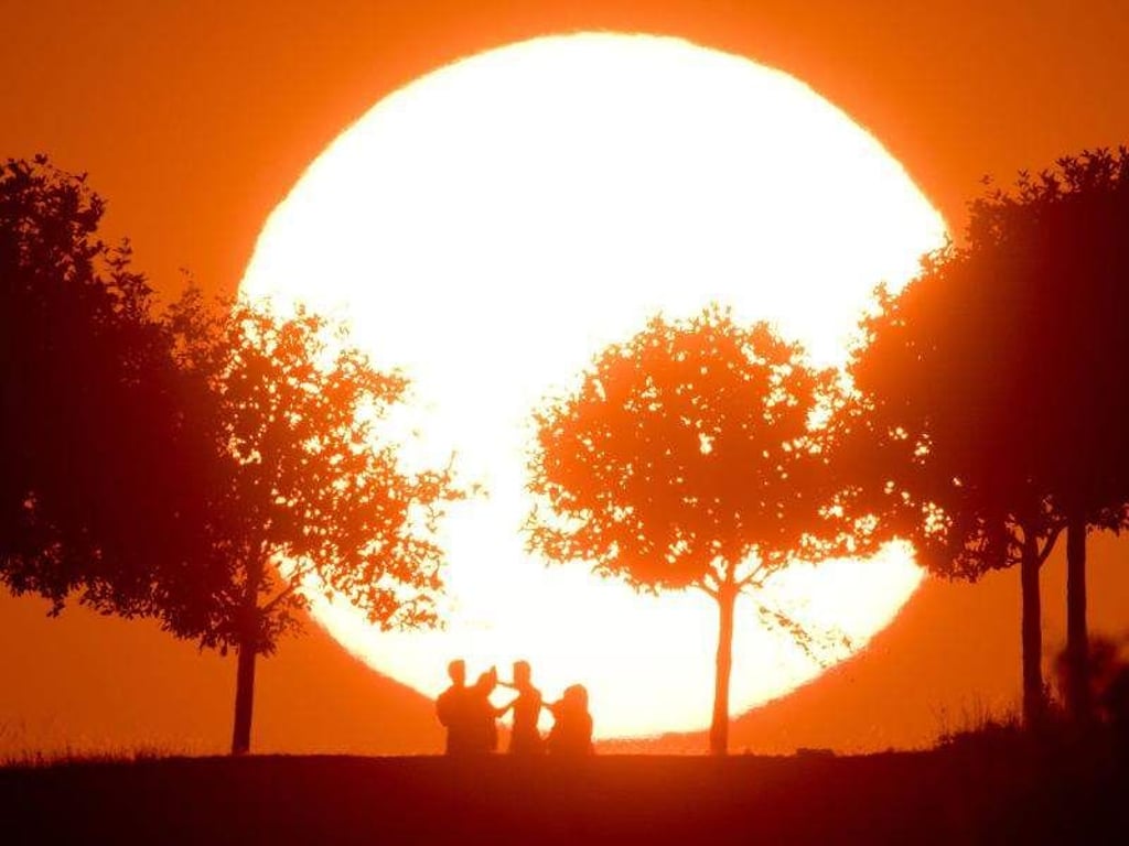 Menschen stehen vor einer untergehenden Sonne. Foto: Julian Stratenschulte/Archiv