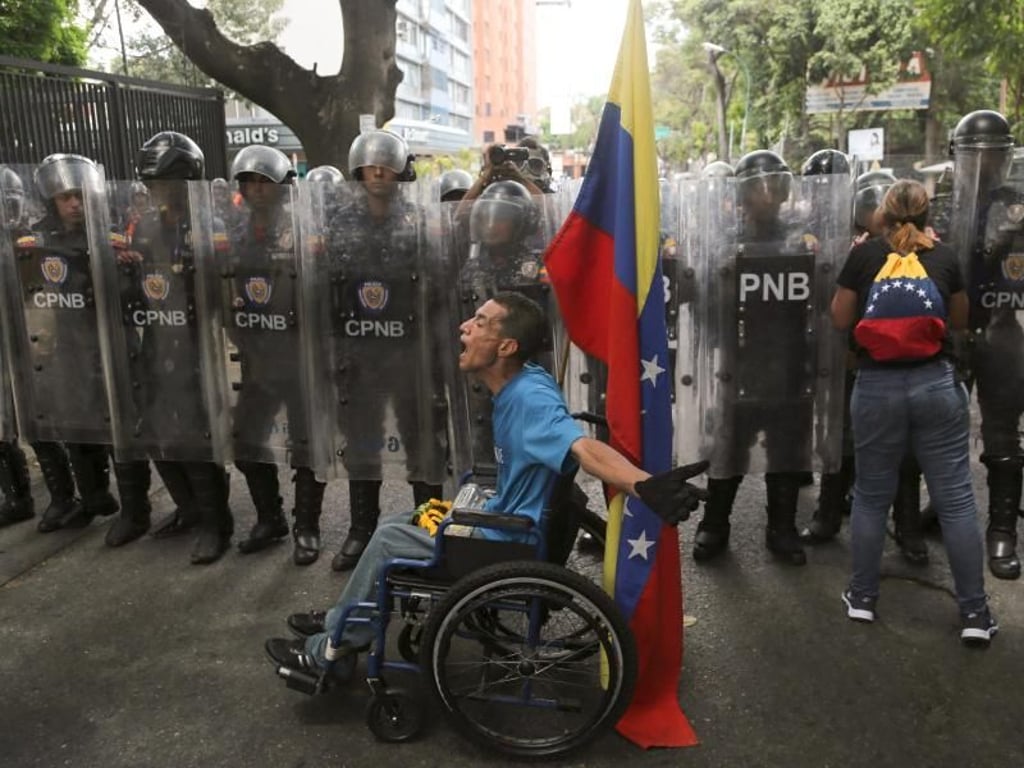 Ungleiche Machtverhältnisse: Ein Demonstrant im Rollstuhl beschimpft Polizisten, die ihn nicht zu einer Demonstration gegen Präsident Maduro durchlassen wollen. Foto: Fernando Llano/AP