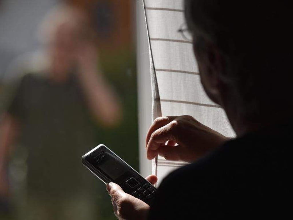 Eine Frau steht mit einem Telefon am Fenster, vor dem ein Mann steht (gestellte Szene). Foto: Angelika Warmuth/Archivbild