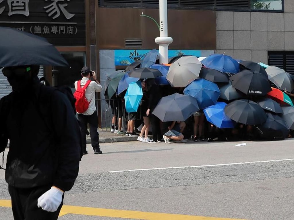 Die Schirme von Hongkong: Regierungskritische Demonstranten schützen sich damit nicht nur vor Tränengas, sondern auch vor Überwachungskameras. Hier versuchen sie, eine Kamera zu demontieren. Foto: Kin Cheung/AP