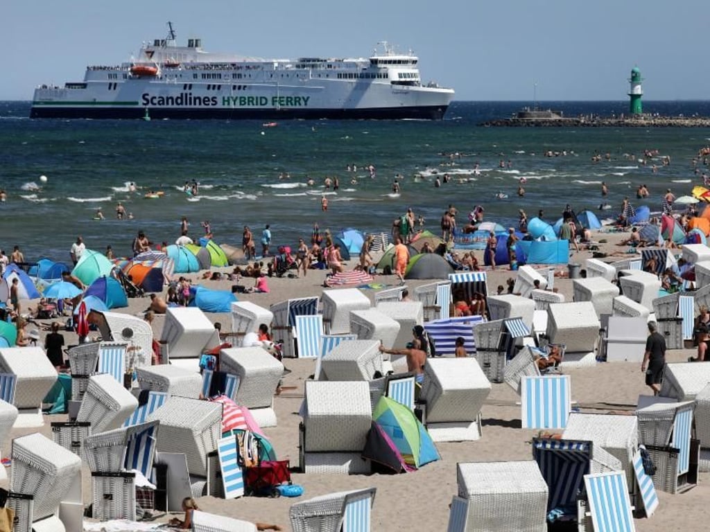 Hochbetrieb am Ostseestrand von Warnemünde, während im Hintergrund die Scandlines-Fähre «Copenhagen» einläuft. Foto: Bernd Wüstneck