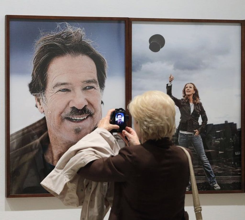 Porträts der Schauspieler Götz George (l) und Katja Flint werden am 08.10.2013 im Kunstmuseum "Kloster Unser Lieben Frauen" in Magdeburg (Sachsen-Anhalt) von einer Besucherin der Eröffnung der Ausstellung "Stand der Dinge" fotografiert. Bis zum 06.01.2014 werden dort 100 Lichtbilder des Fotografen Jim Rakete von Filmschaffenden aus dem deutschsprachigen Raum präsentiert. Foto: Jens Wolf/dpa +++(c) dpa - Bildfunk+++