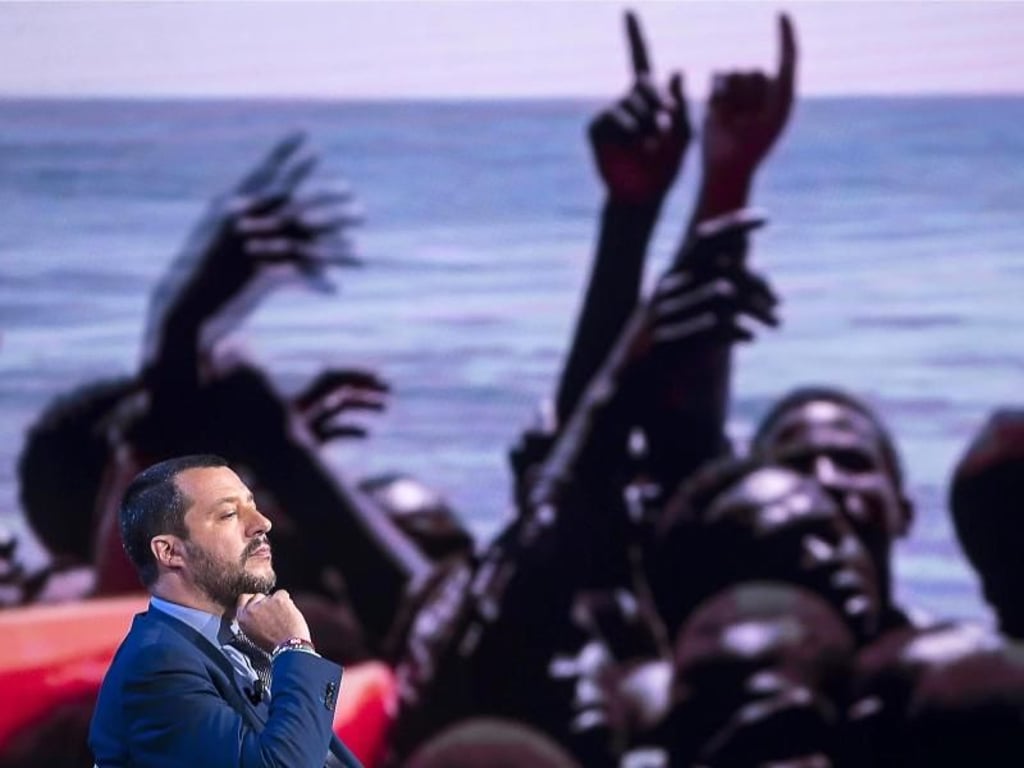 Italiens Innenminister Salvini vergangene Woche zu Gast in einer Sendung des Senders RAI, während im Hintergrund ein Bild von Migranten gezeigt wird. Foto: Angelo Carconi/ANSA/AP