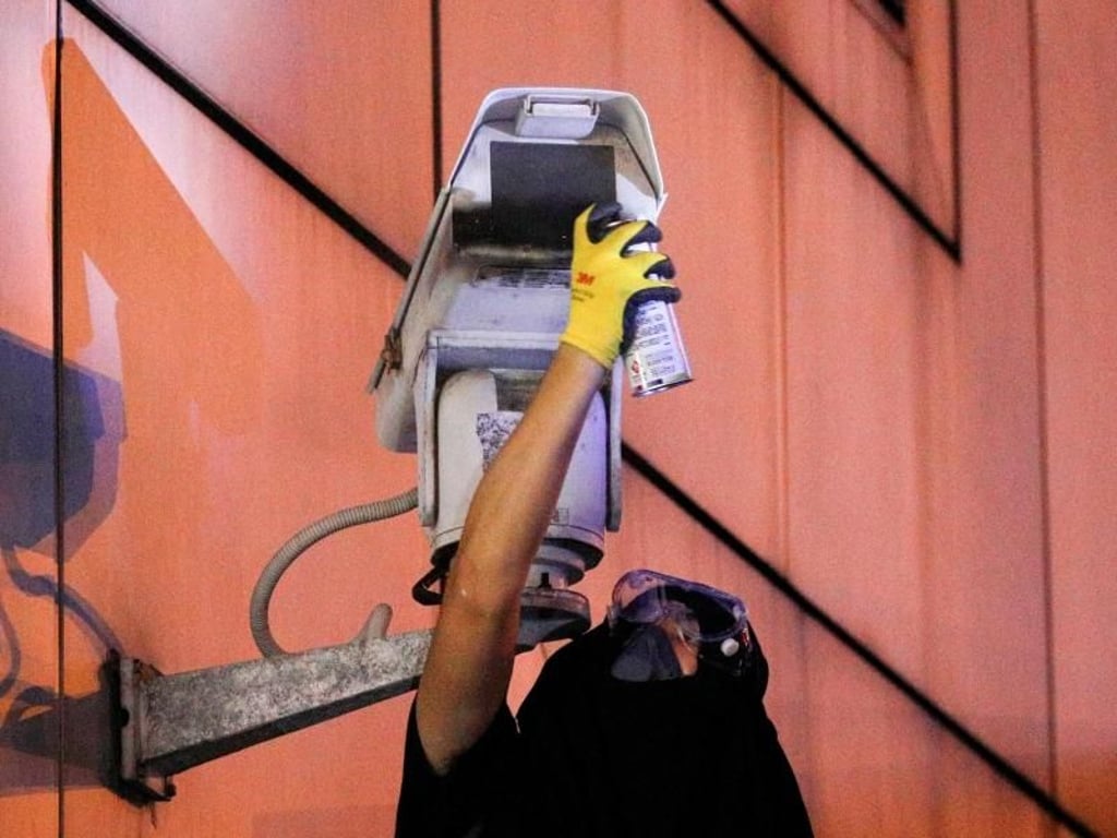 Ein Demonstrant besprüht eine Überwachungskamera vor einem chinesischen Regierungsgebäude. Foto: Bobby Yip/AP
