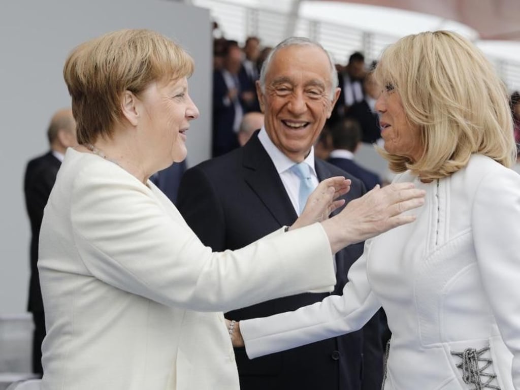 Bundeskanzlerin Angela Merkel (l) und Brigitte Macron begrüßen sich. Viele europäische Staats- und Regierungschefs verfolgen auf der Ehrentribüne die Militärparade. Foto: Kamil Zihnioglu/AP