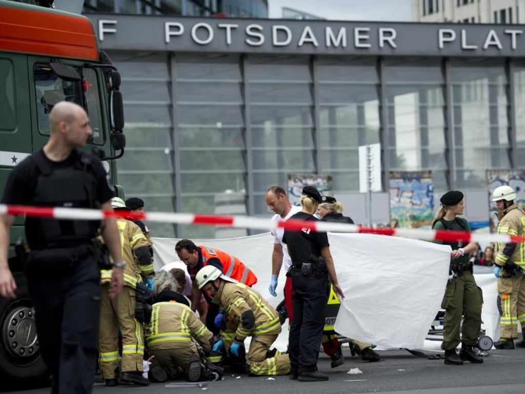 Rettungskräfte helfen auf der Straßenkreuzung am Potsdamer Platz in Berlin einem verletzten Radfahrer, der unter einem Lastwagen liegt. Foto: Daniel Reinhardt