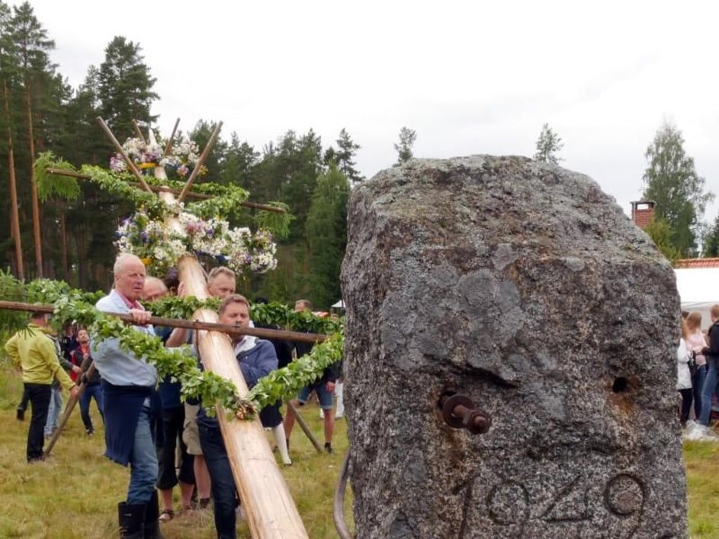 Die Männer richten den Midsommarbaum auf, dann befestigen sie ihn mit einem Stahlseil und Schrauben an dem Stein. Foto: Isabelle Modler