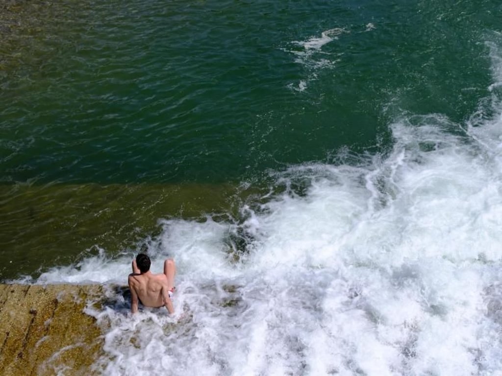 München: Ein Mann kühlt sich bei sommerlichen Temperaturen an einem Wasserfall in der Isar ab. Foto: Sven Hoppe