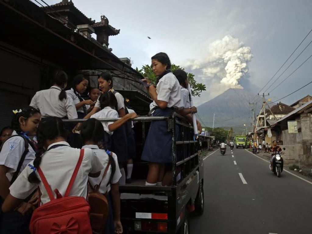 Auf dem Weg zur Schule: Balinesische Jugendliche klettern auf einen Pick-up, während der Mount Agung im Hintergrund Rauch und Asche spuckt. Foto: Firdia Lisnawati