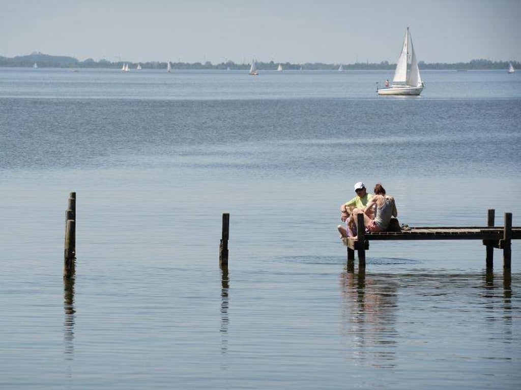 Eine Familie sitzt nahe der Badeinsel auf einem Steg. Foto: Susann Prautsch/Archiv