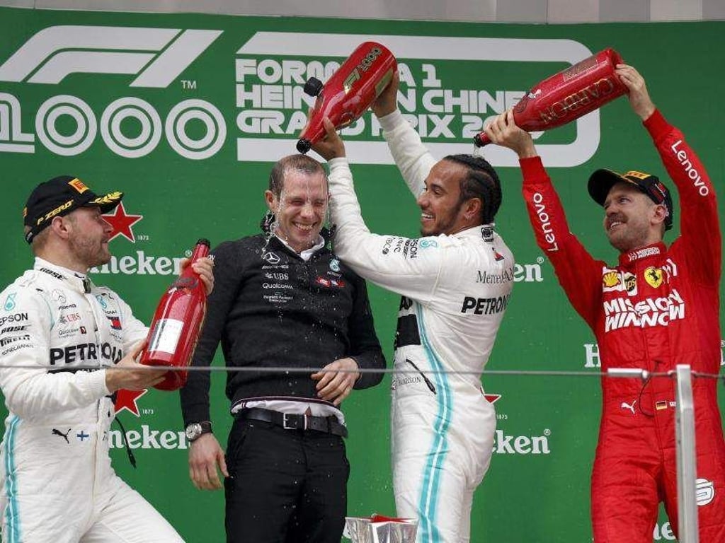 Sebastian Vettel (r) spendiert für Sieger Lewis Hamilton eine Champagner-Dusche. Foto: Andy Wong/AP