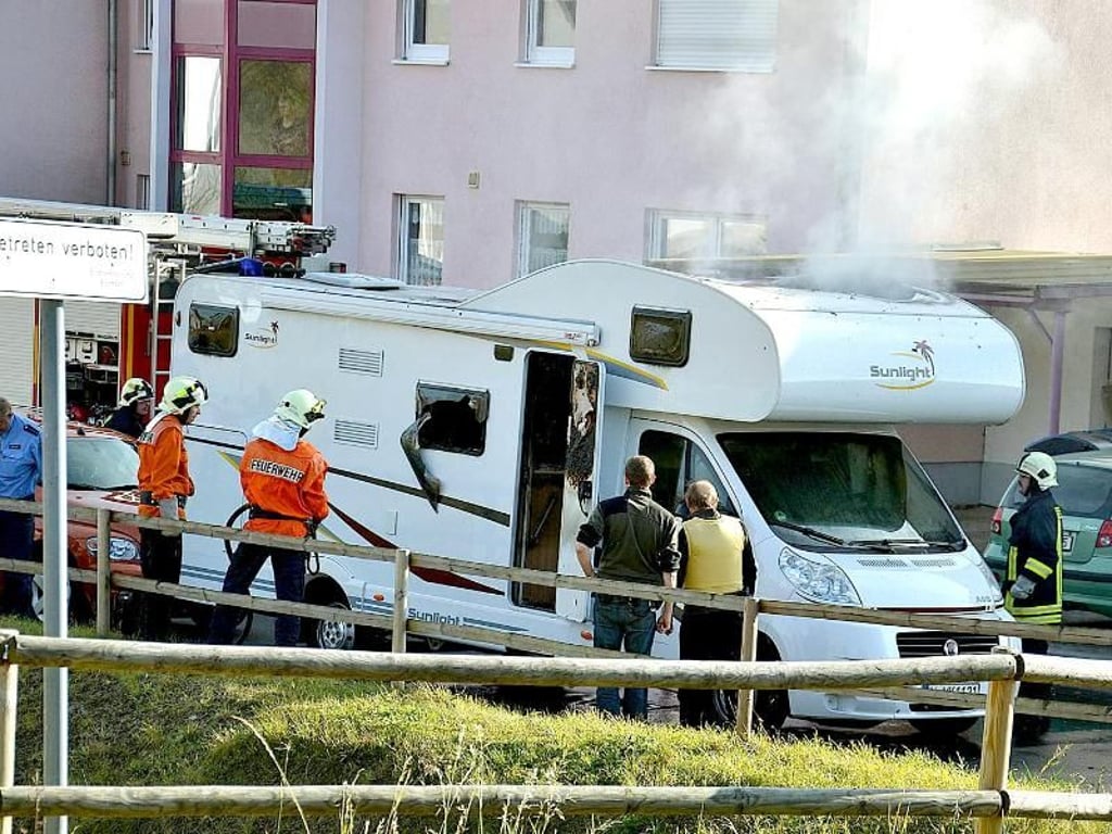 Feuerwehrleute und Polizisten vor dem qualmenden Wohnmobil, in dem die Leichen von Uwe Mundlos und Uwe Böhnhardt gefunden wurden. Foto: Carolin Lemuth/Archiv