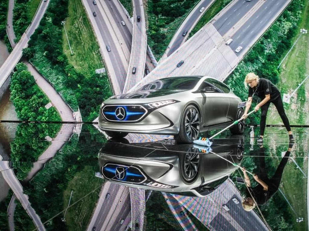 Eine Mitarbeiterin wischt am Stand von Mercedes unter einem Elektro-Konzept-Fahrzeug namens EQ A den Boden. Foto: Frank Rumpenhorst