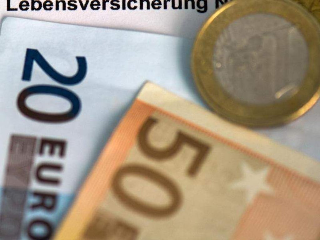 Auf einem Schein für eine Lebensversicherung liegen Münzen und Geldscheine. Foto: Arno Burgi/Archiv