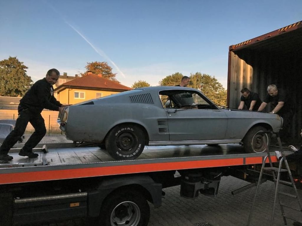 Unboxing: Helfer rollen einen frisch importierten Ford Mustang aus dem Container. Foto: Dieter Thiel/USCars24/dpa-tmn