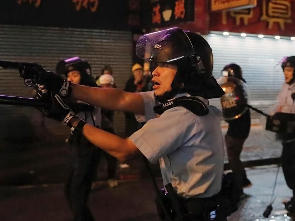Ein Polizist zielt mit seiner Waffe auf Demonstranten. Foto: Kin Cheung/AP