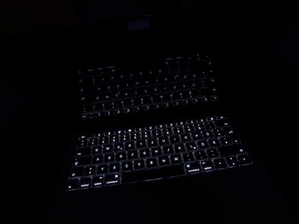 Ein Macbook dessen leuchtende Tastatur sich im Monitor spiegelt steht im Dunklen. Foto: Karl-Josef Hildenbrand/Architektur