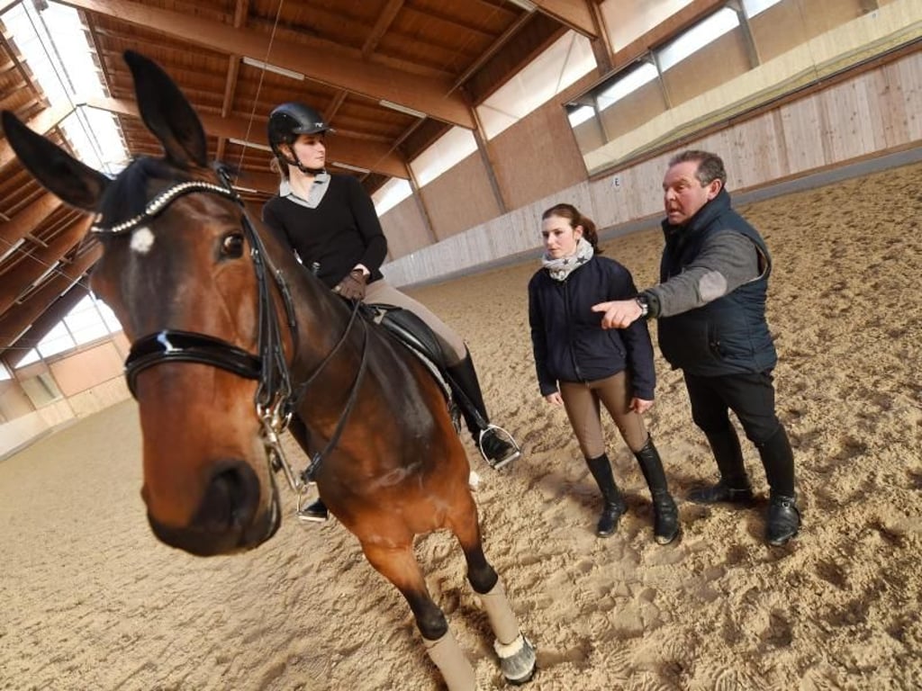 Die Zügel nicht zu locker lassen: Ausbilder Ulrich Rasch erklärt Pferdewirtin Sophia Mann (M), worauf sie beim Reitunterricht achten muss. Mann arbeitet auf Gut Riedhausen in Brunnthal bei München. Foto: Tobias Hase