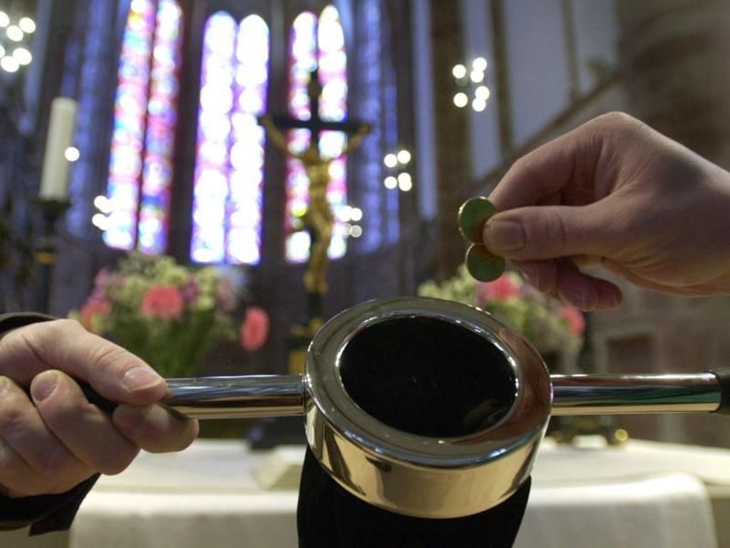Ein Kirchenbesucher (r) steckt einige Münzen in einen Klingelbeutel. Foto: Werner Baum