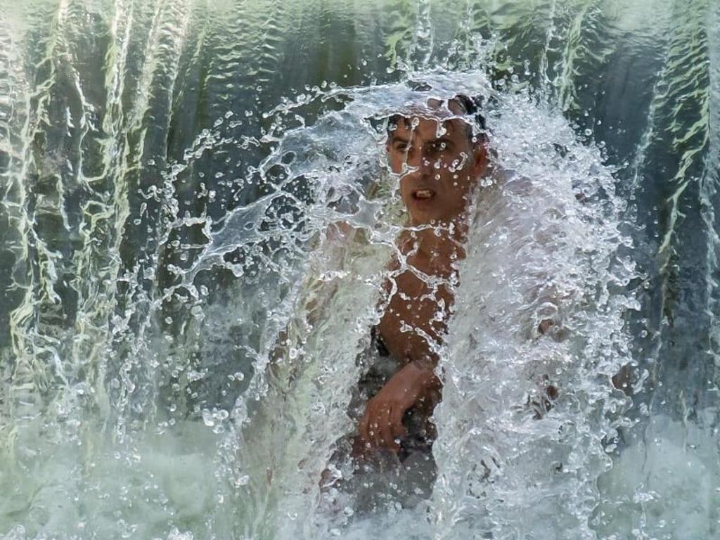 Ein Mann kühlt sich an einem kleinen Wasserfall im Eisbach im Englischen Garten ab. Foto: Peter Kneffel
