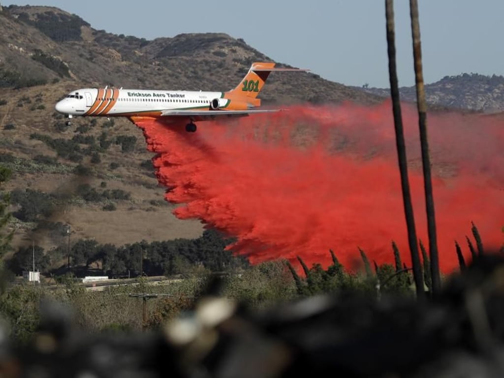 Ein Löschflugzeug wirft seine rot gefärbte Wasserladung ab. Hunderttausende Menschen mussten ihre Häuser bereits verlassen. Foto: Gregory Bull