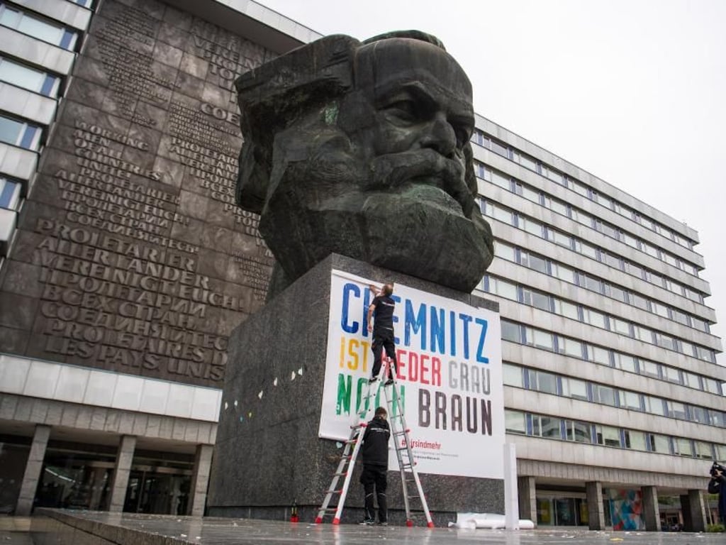1. September: Zwei Männer befestigen am Karl-Marx-Denkmal ein Plakat mit der Aufschrift «Chemnitz ist weder grau noch braun». Foto: ZB