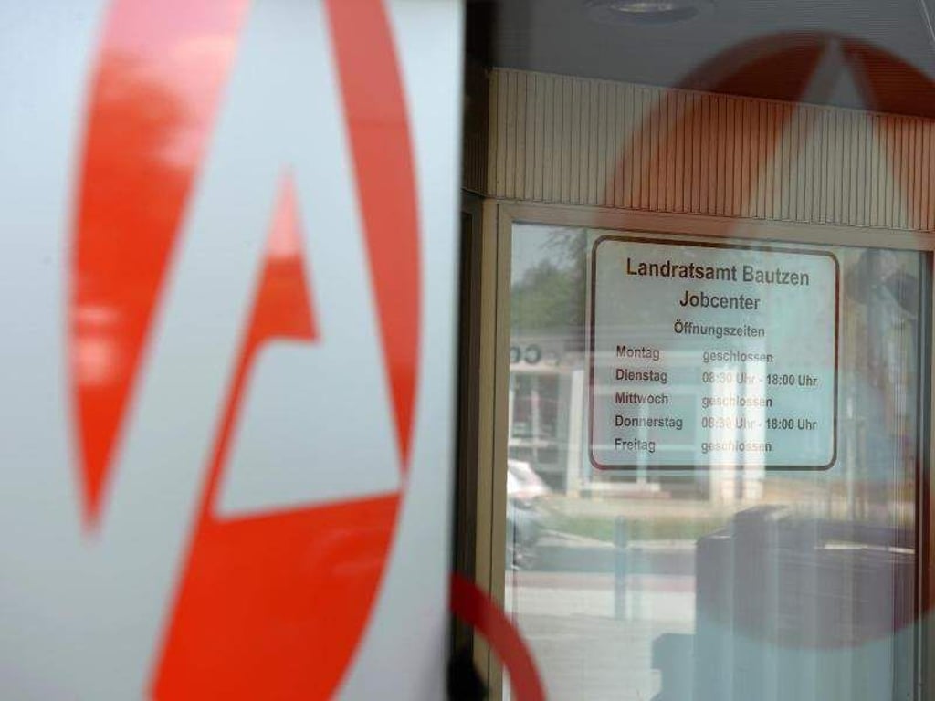 Das Logo der Agentur für Arbeit spiegelt sich an einer Eingangstür. Foto: Jens Kalaene/Archiv