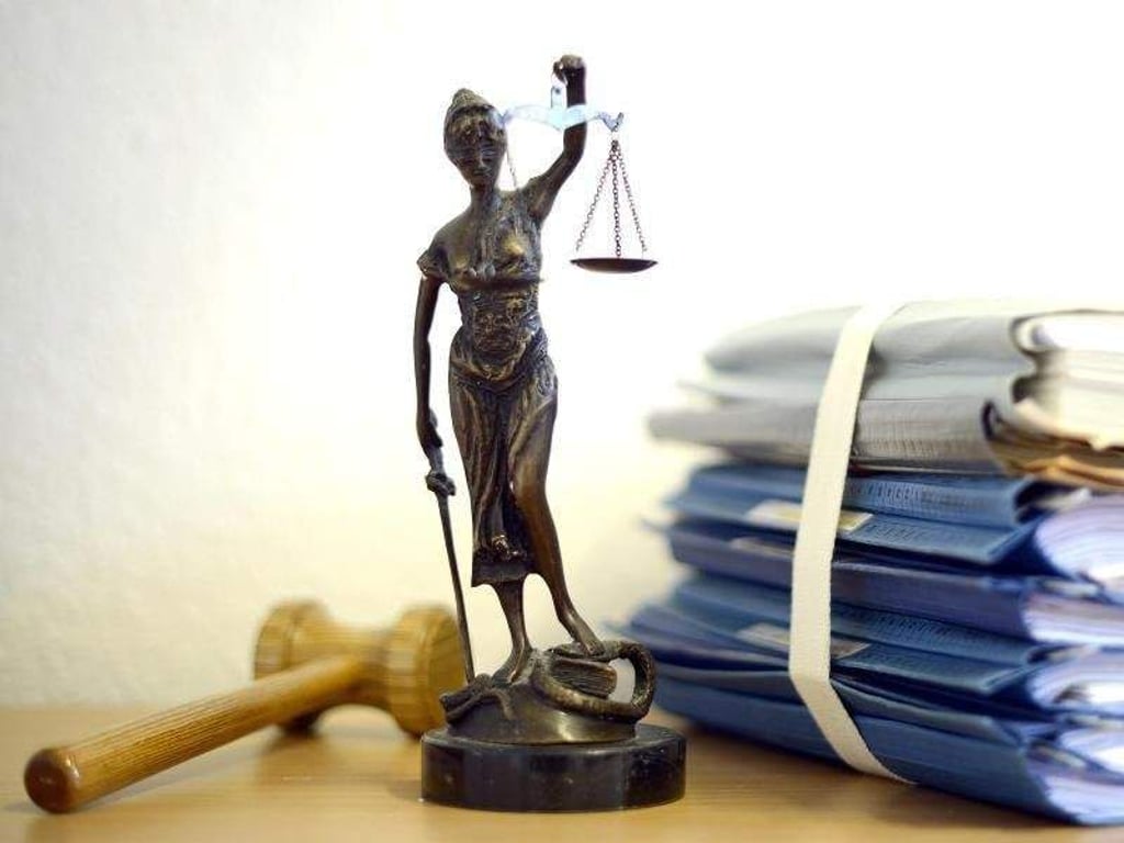 Die modellhafte Nachbildung der Justitia steht in einem Raum eines Richters neben einem Holzhammer und einem Aktenstapel. Foto: Volker Hartmann/Illustration