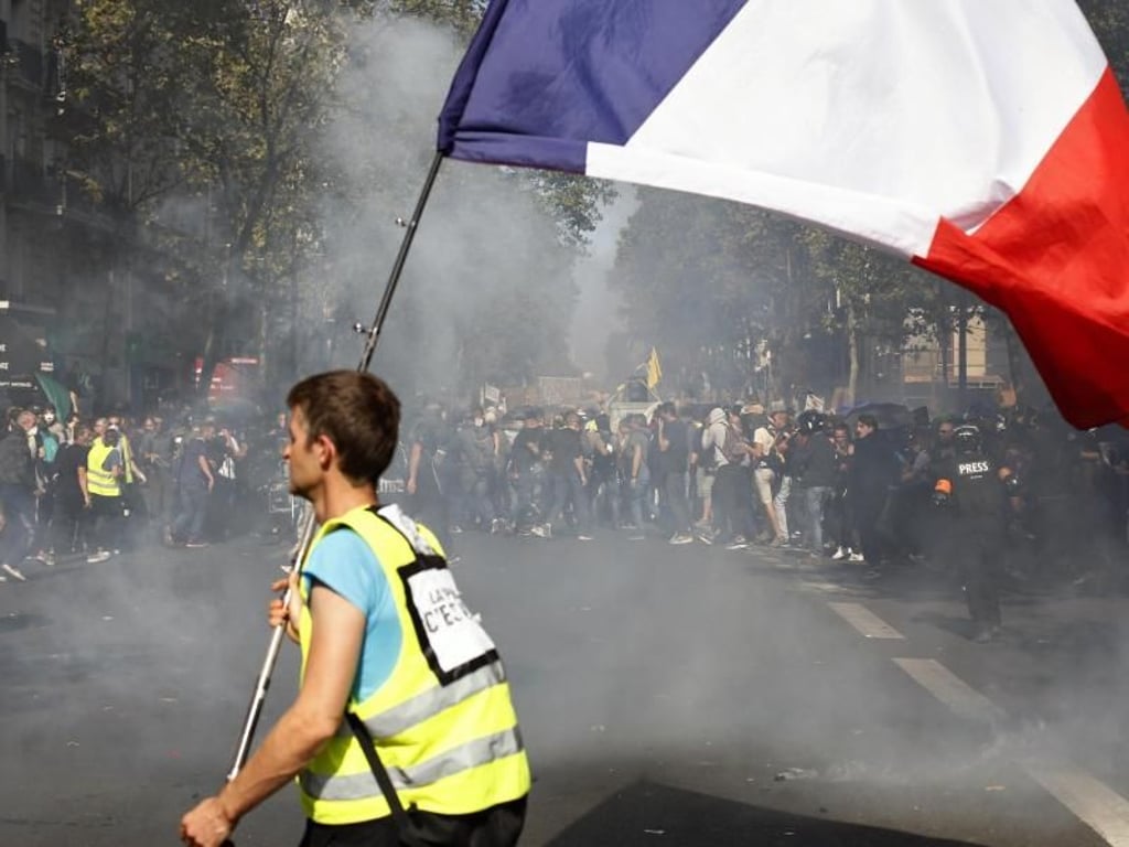 Ein Demonstrant mit gelber Weste trägt bei den Protesten eine französische Flagge. Foto: Thibault Camus/AP