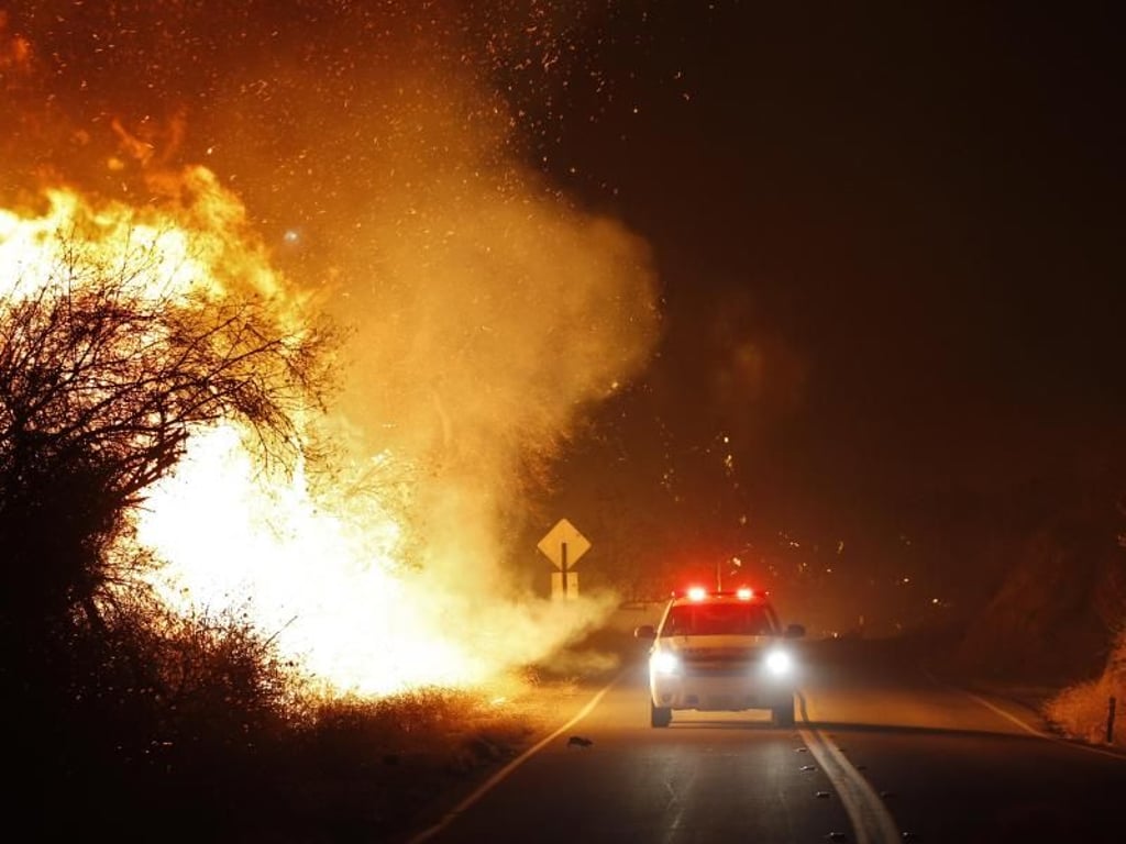 Einsatzkräfte der Feuerwehr fahren auf der West Lilac Road neben: Flammen schlagen ihnen entgegen. Foto: K.C. Alfred