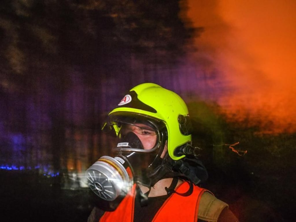 Mit Atemschutzmaske kommt ein Feuerwehrmann aus einem brennenden Waldstück. Rund 300 Einsatzkräfte bekämpfen die Flammen. Foto: Patrick Pleul