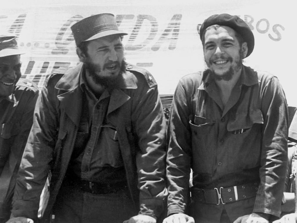 Fidel Castro (l), damals Ministerpräsident von Kuba, und der legendäre Guerilla-Führer Ernesto «Che» Guevara sehen auf einem Fliegerstützpunkt im August 1960 einer Bauern-Militärparade zu. Foto: dpa