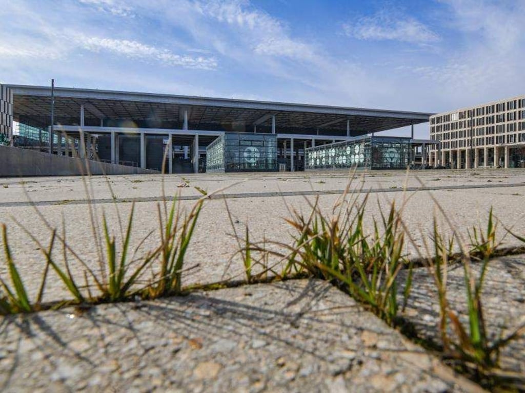 Gras wächst zwischen den Fugen auf einem Platz vor dem Terminal des Hauptstadtflughafens BER. Foto: Patrick Pleul