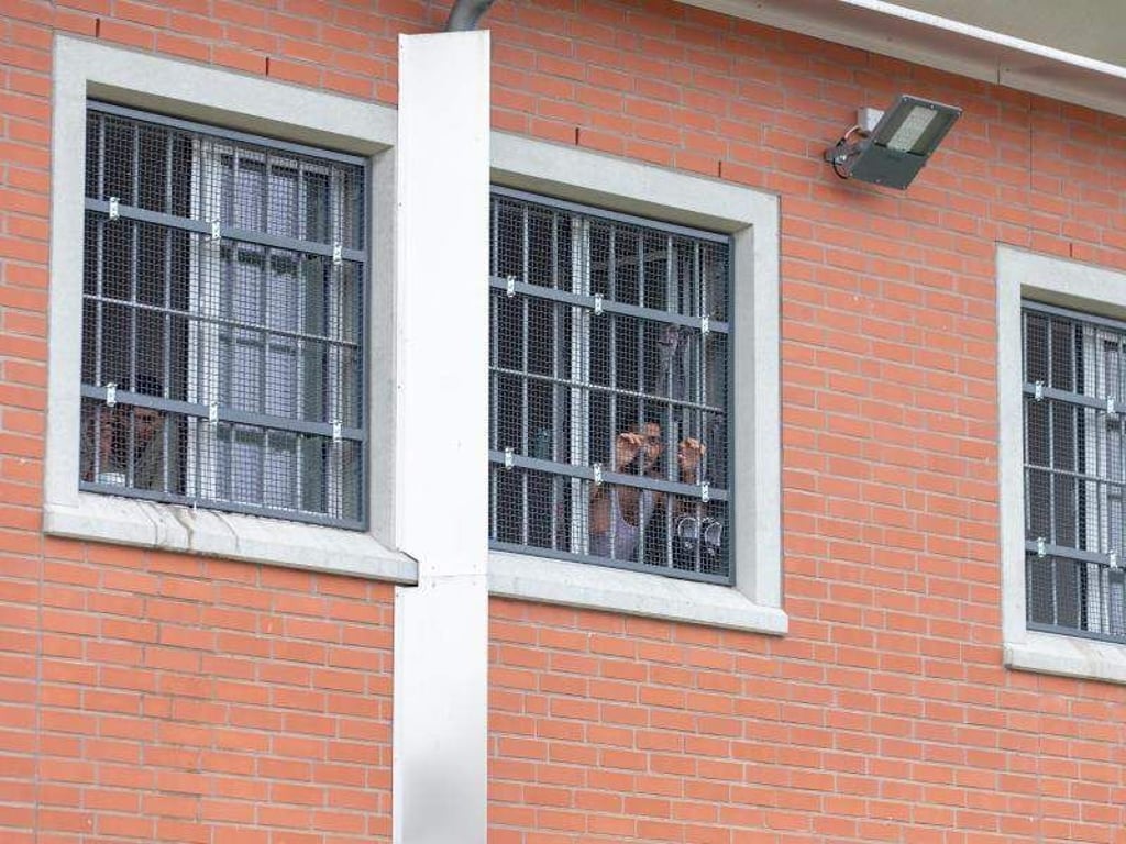 Insassen blicken durch vergitterte Fenster in der Unterbringungseinrichtung für Ausreisepflichtige. Foto: Friso Gentsch/Archiv
