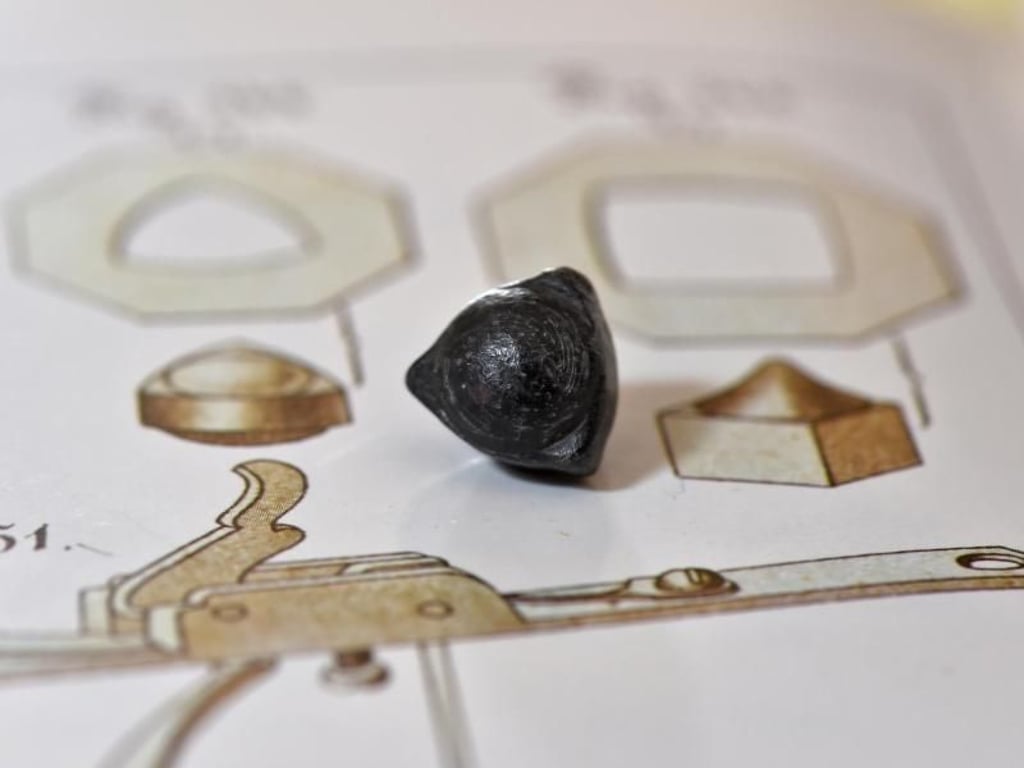 Ein dreieckiges Geschoss auf einem Buch über historische Munition, Geschosse und Gewehre. Foto: Felix Kästle