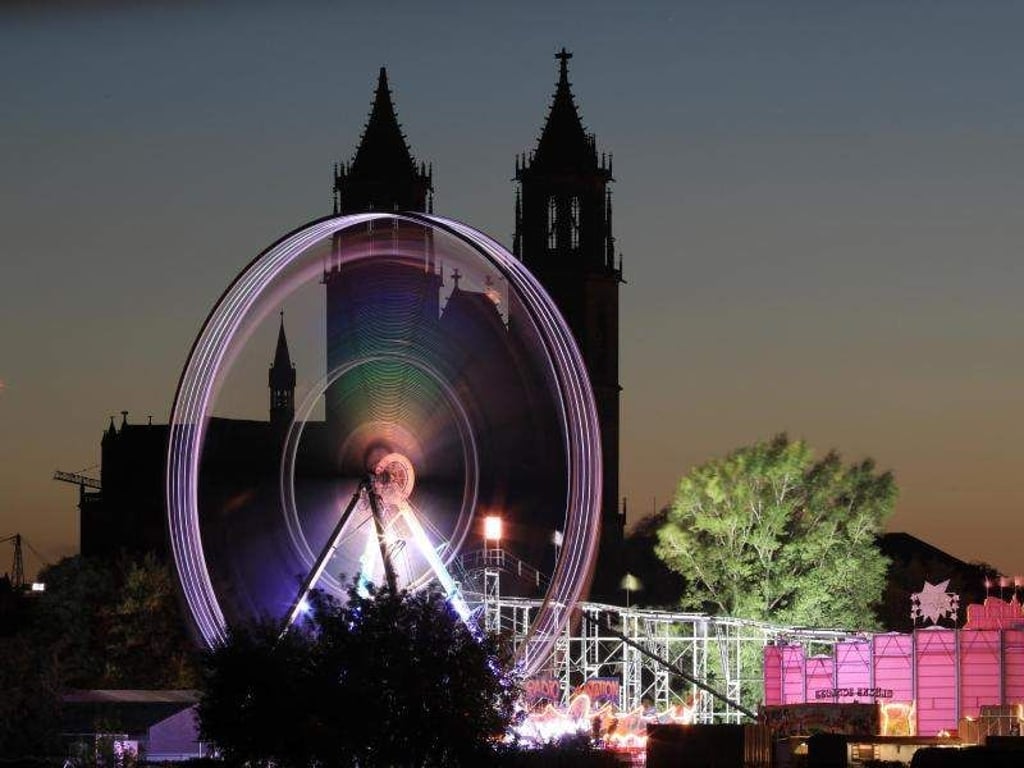 Ein Riesenrad erstrahlt vor der Silhouette des Domes in Magdeburg auf der 108. Magdeburger Herbstmesse. Foto: Peter Gercke/Archiv