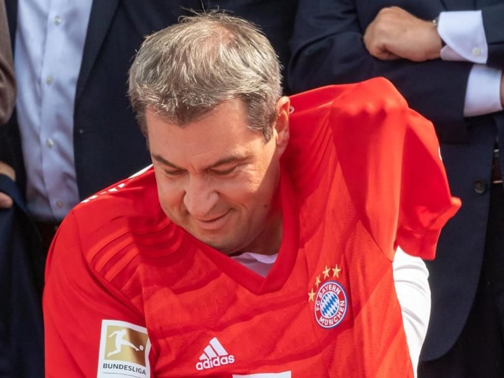 Bayerns Ministerpräsident Markus Söder zwängt sich in ein Trikot des FC Bayern München, das ihm zuvor Uli Hoeneß überreicht hat. Foto: Peter Kneffel