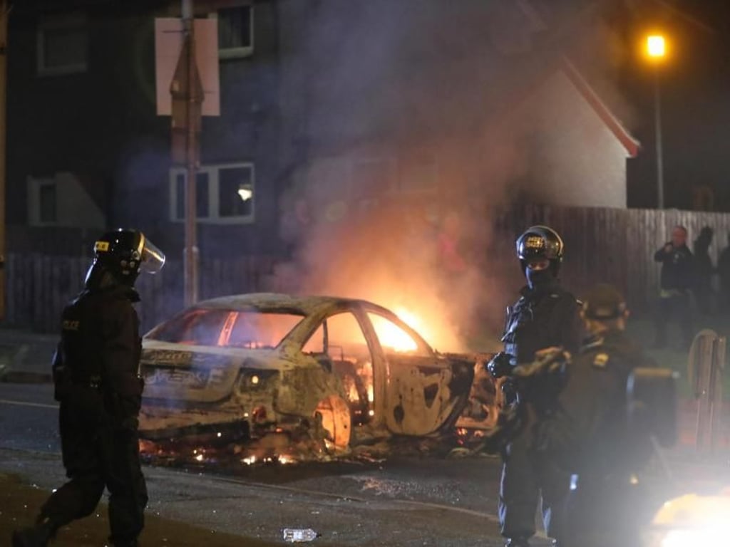 Polizisten vor einem brennenden Auto. Foto: Niall Carson/PA Wire