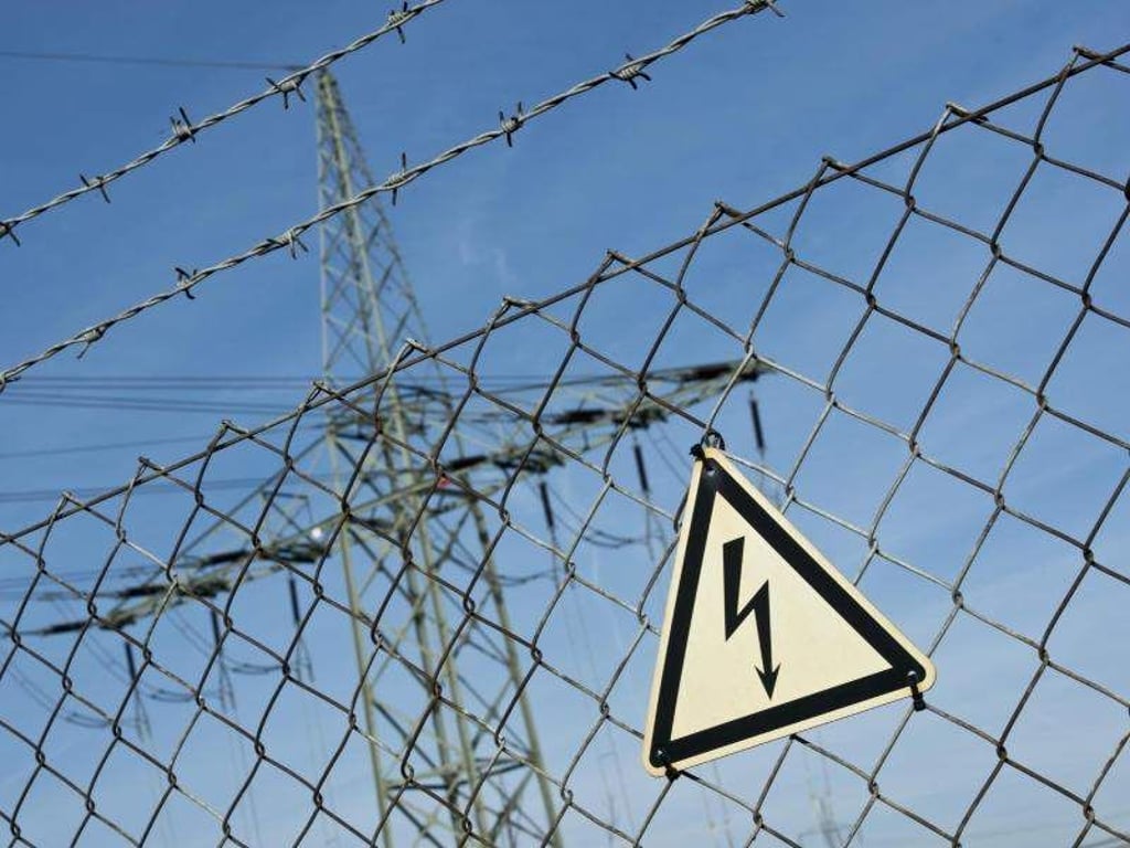 Ein Gefahrenschild für Elektrizität ist vor einer Stromtrasse zu sehen. Foto: Daniel Naupold/Archiv