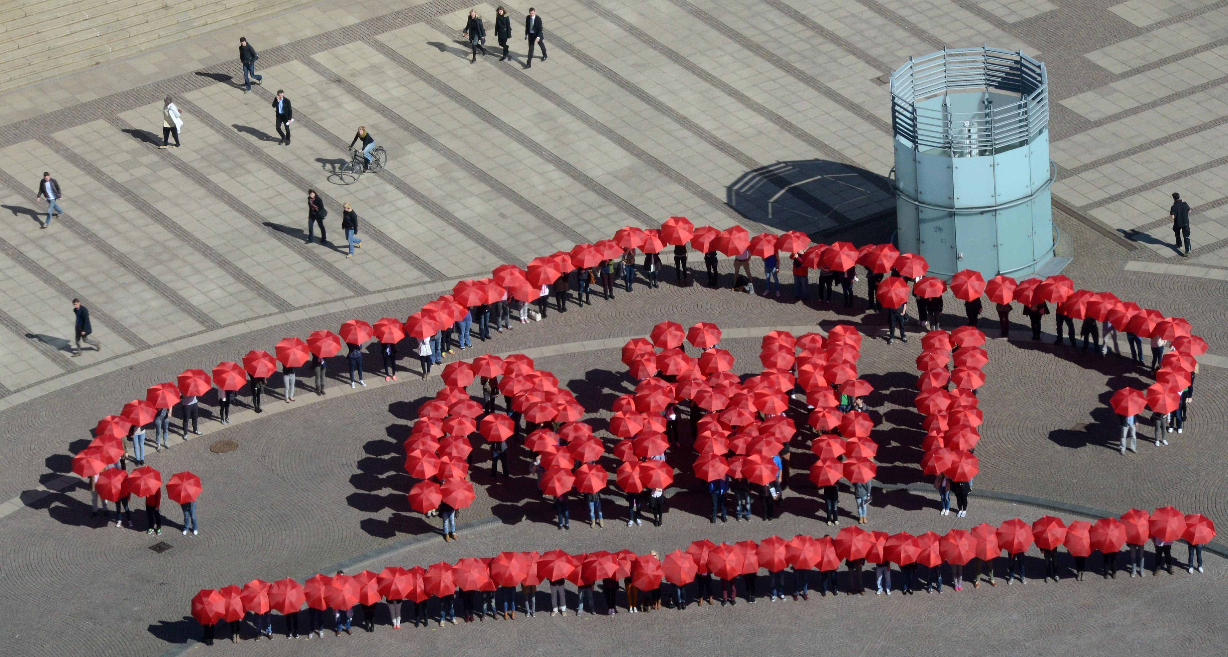 Über 180 Mitwirkende mit roten Regenschirmen gestalten im März 2014 das Logo der Automobilmesse AMI auf dem Augustusplatz in Leipzig.