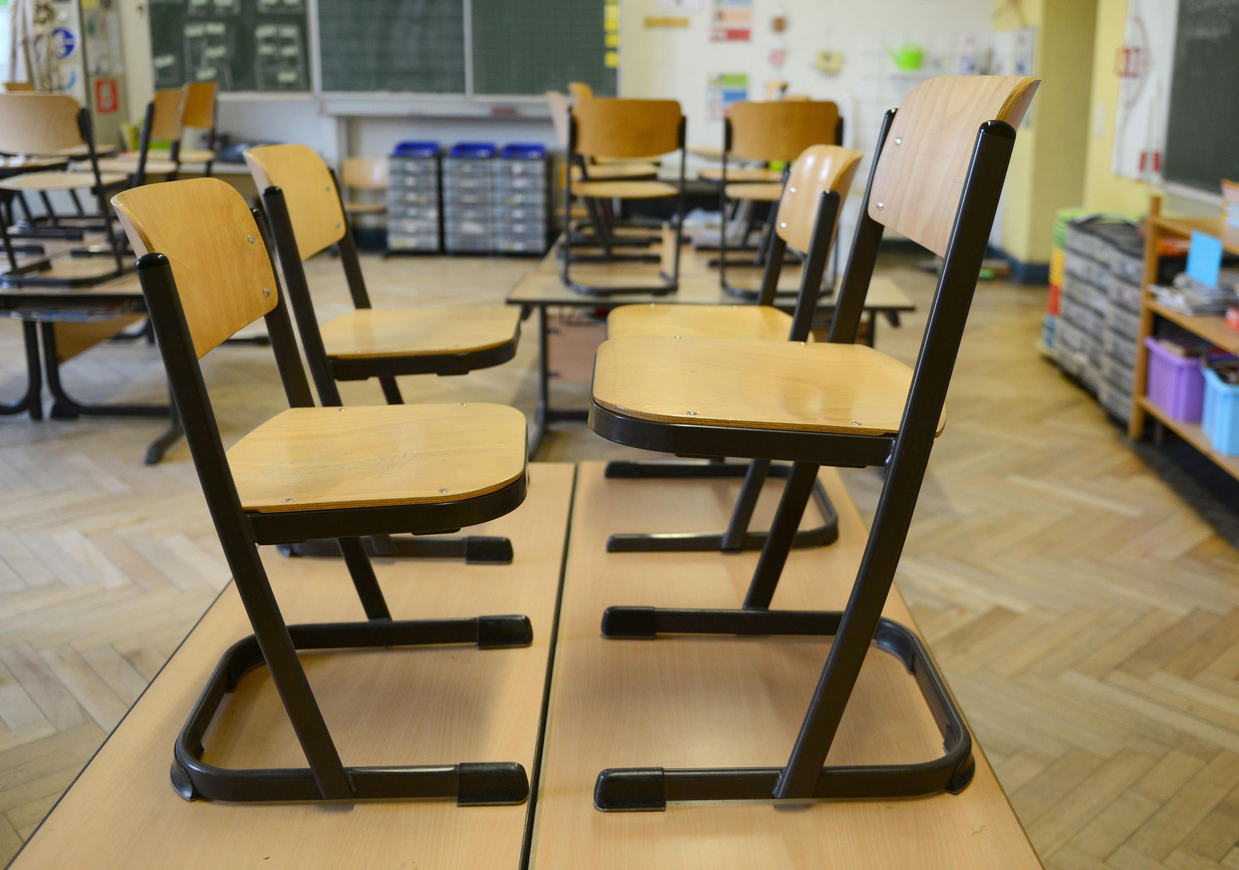Stühle stehen nach Unterrichtsende in einem Klassenraum auf den Schulbänken.