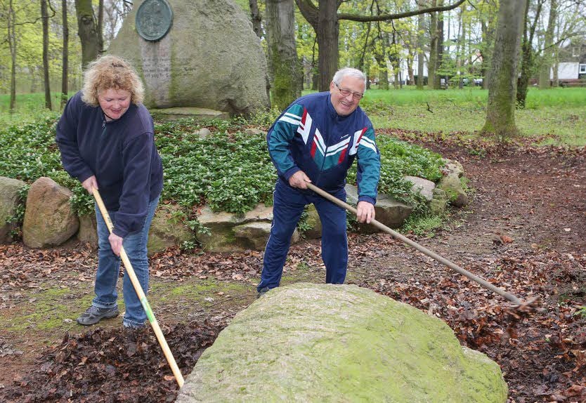 Kerstin Czepluch und Helmut Kusche harken altes Laub am Schillerstein im Klemmbergpark weg.